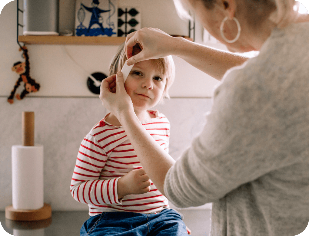 Mother placing an adhesive bandage on daughter’s face to cover a head wound.