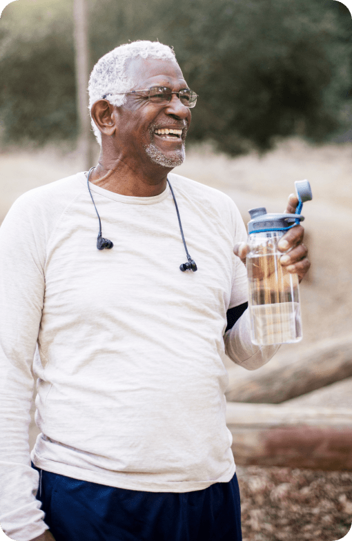 Man smiling and holding a water while taking a walk outdoors.
